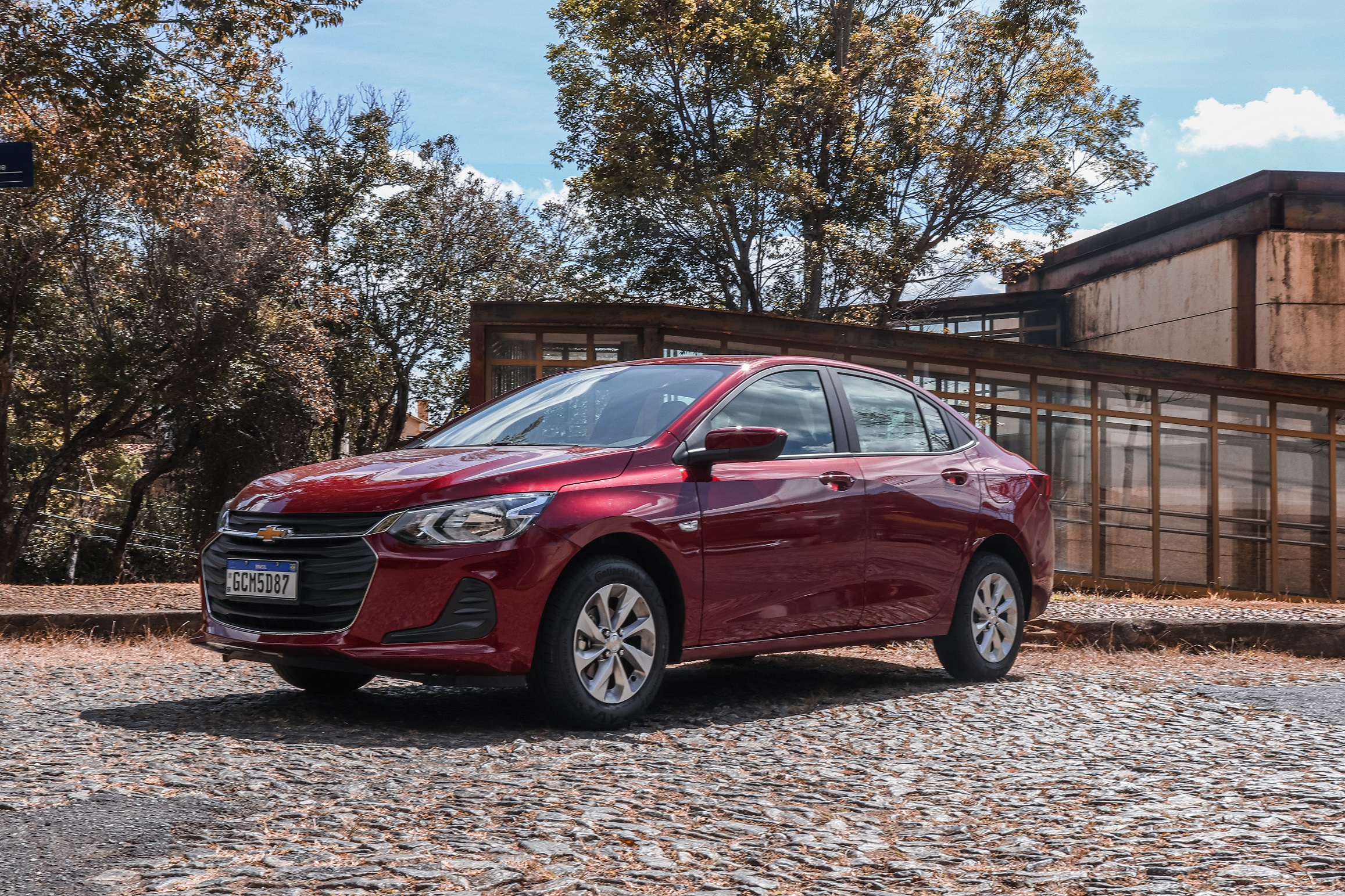 Chevrolet Onix Plus LT 2022 vermelho de frente estacionado em rua arborizada