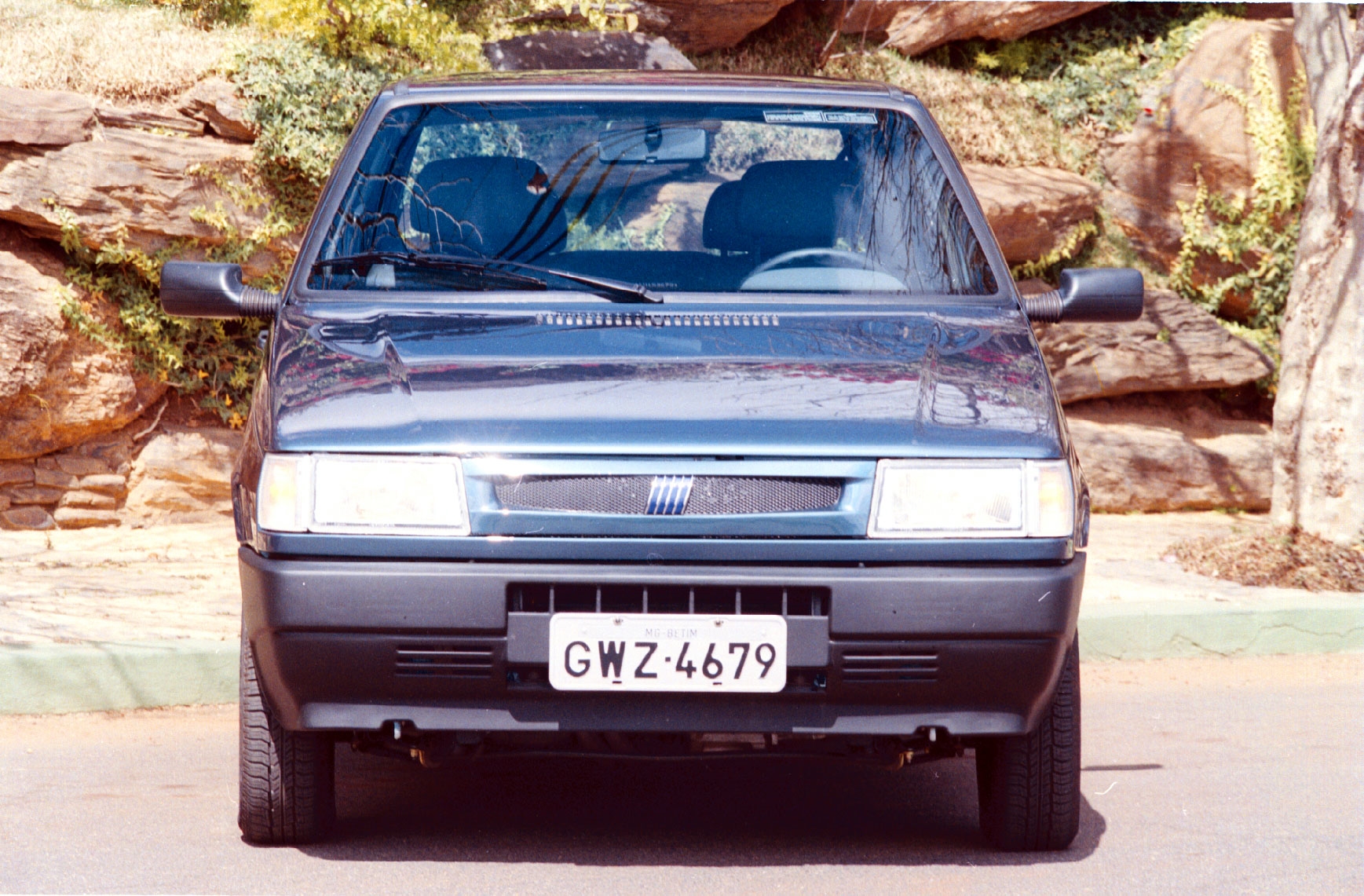 Fiat Uno Mille Smart modelo 2000 azul metálico de frente na frente do muro de pedras