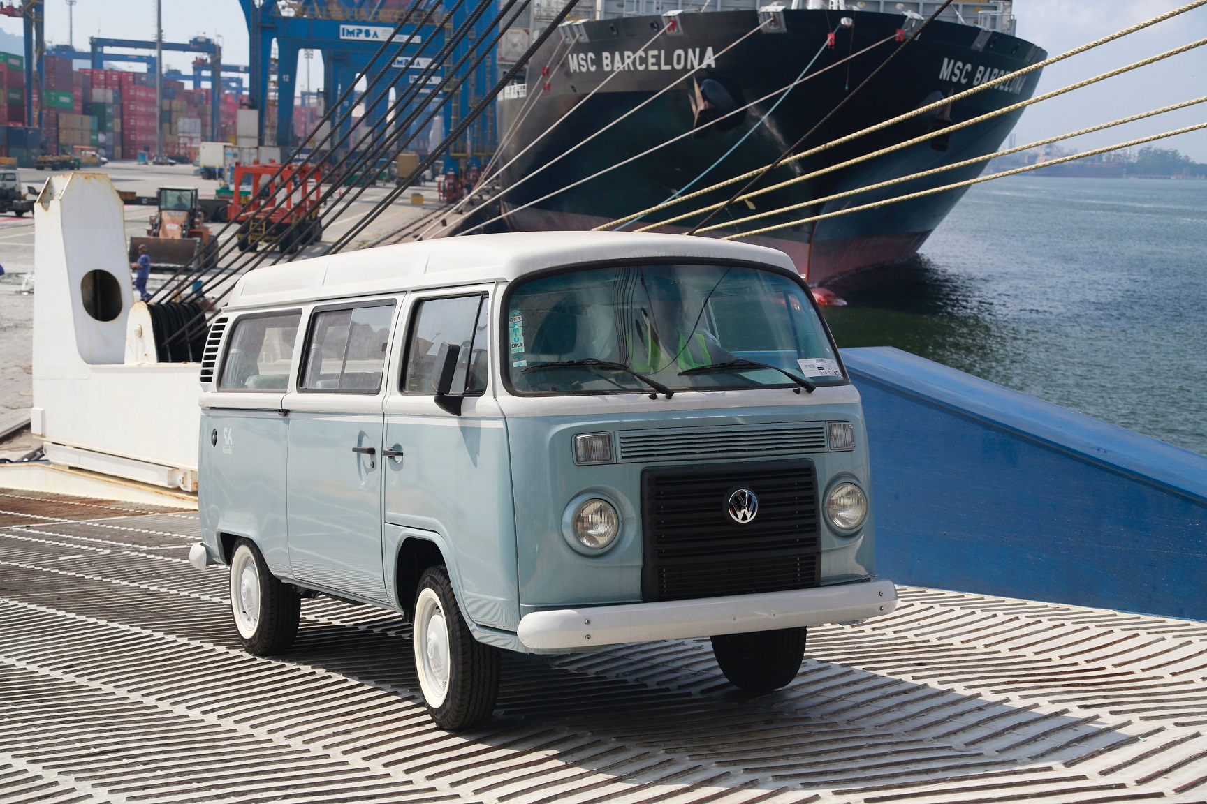 Volkswagen Kombi Last Edition azul e branca de frente com porto ao fundo