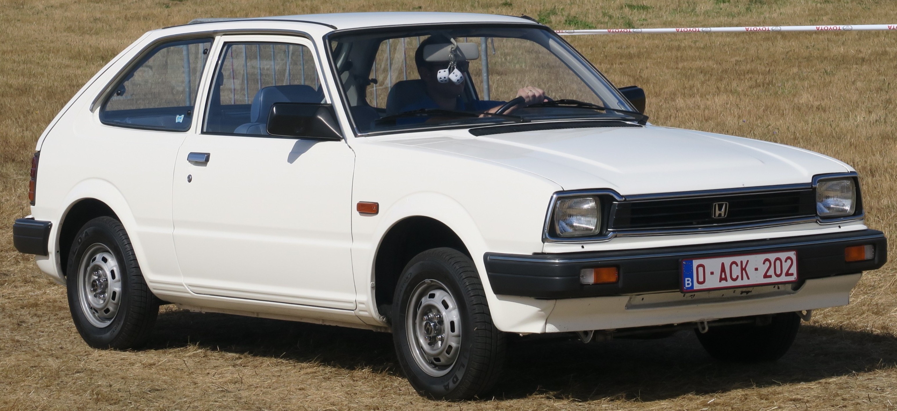Honda Civic 1980. O carro é branco, possui para-choque e grades na cor preta.