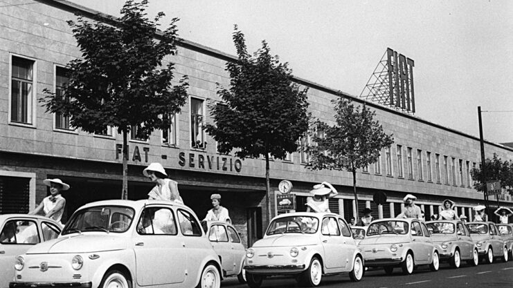 Imagem em preto e branco com fila de carros do modelo Fiat 500. Em todos, há uma mulher levantada e sentada na parte de cima, aberta, do banco traseiro
