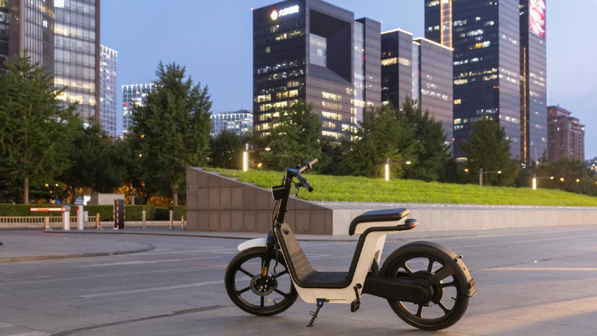 O scooter elétrico Honda MS01 de lado com cena urbana ao fundo.