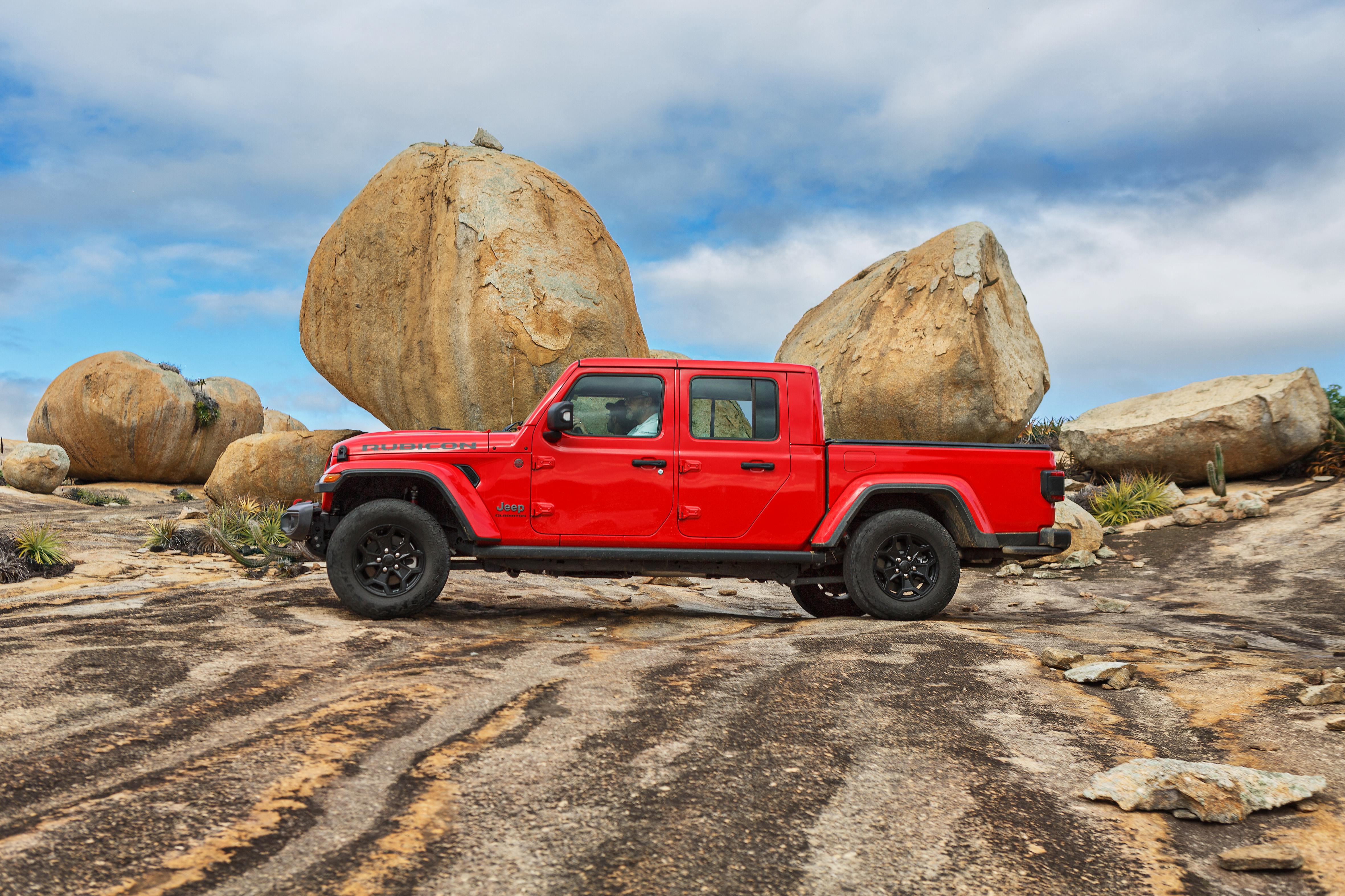Jeep Gladiator Rubicon 2022 vermelho de lado entre grandes pedras.