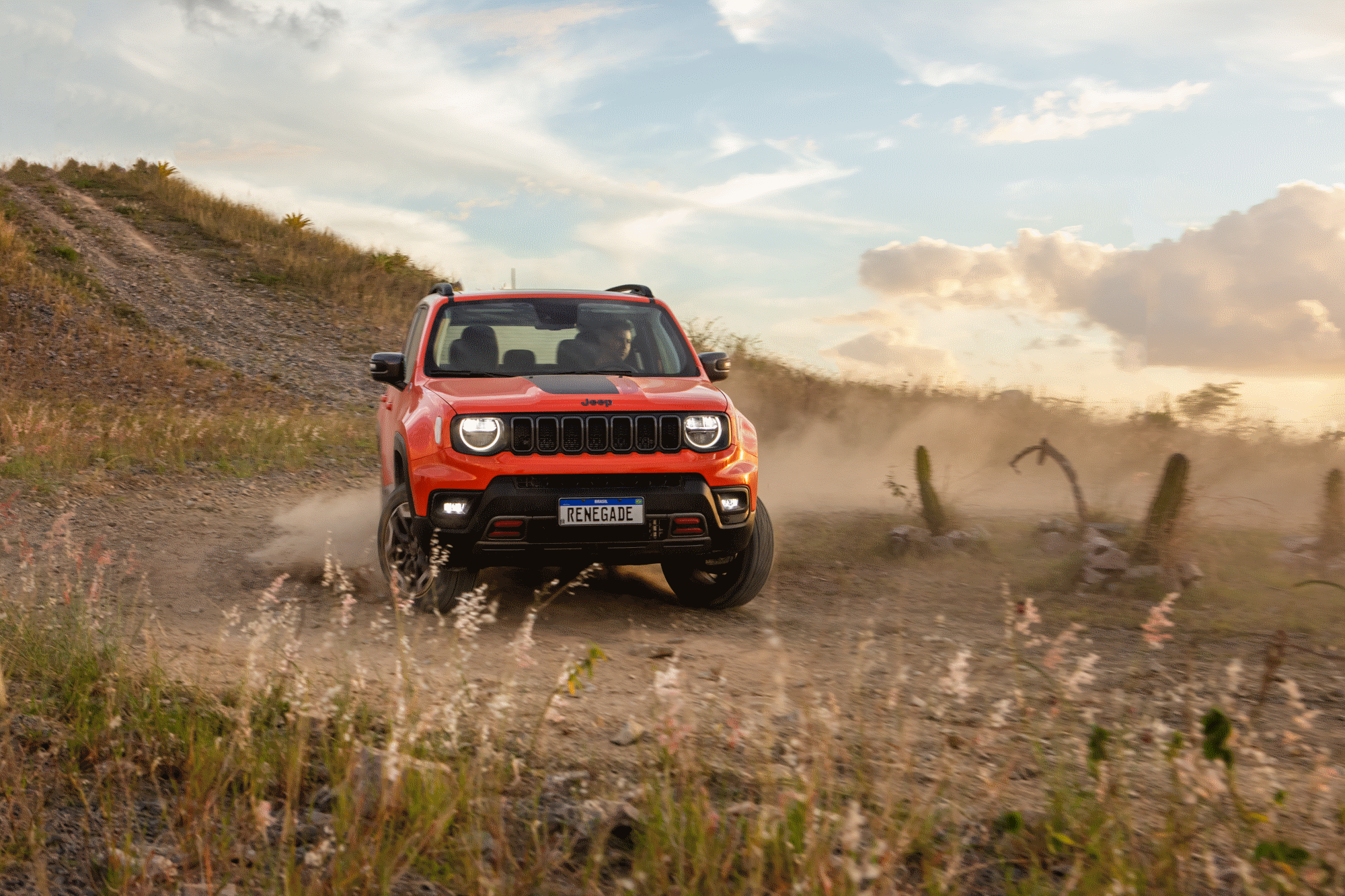 Jeep Renegade laranja visto de frente em meio à paisagem de terra e vegetação rasteira. 