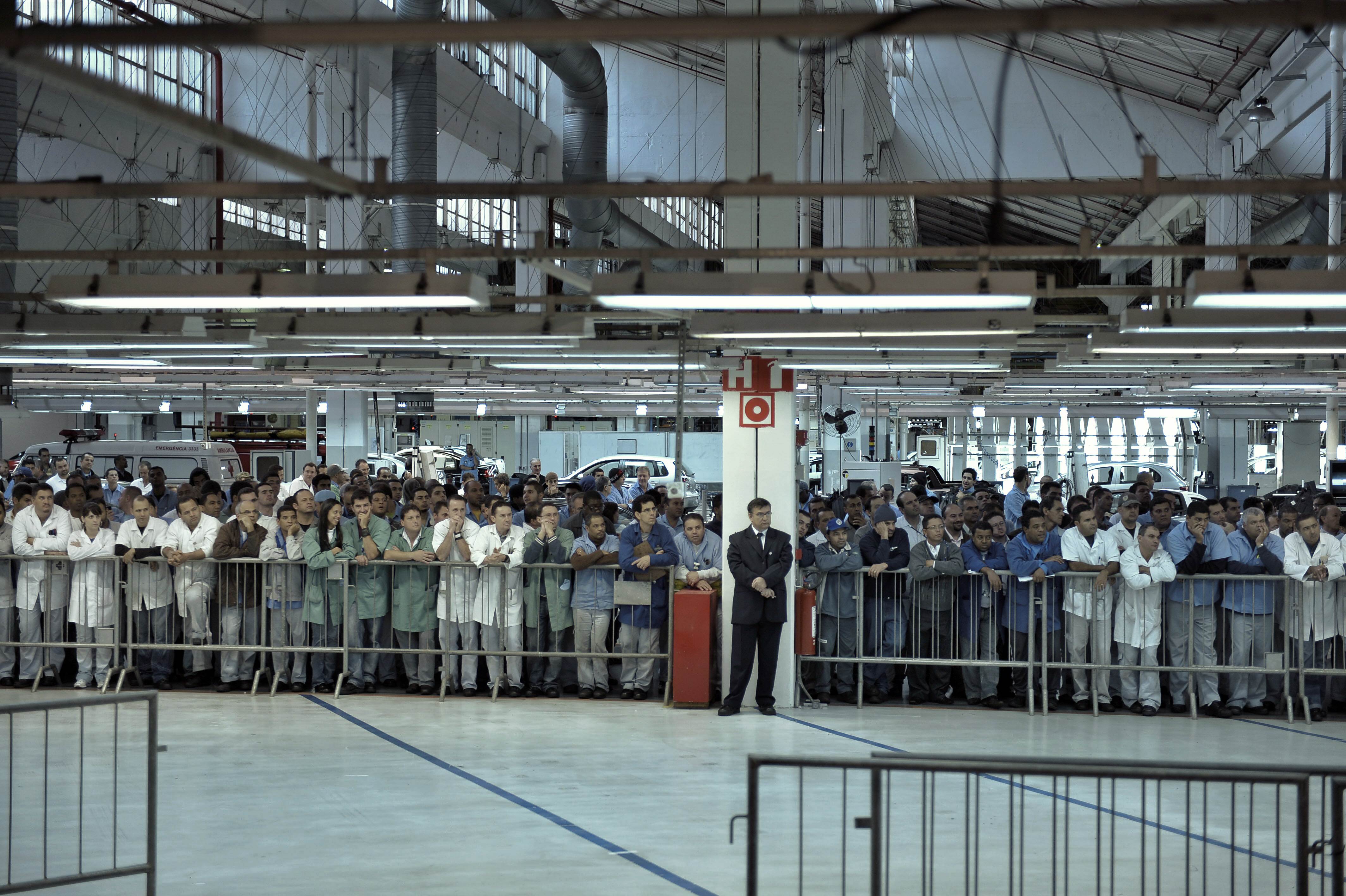 Trabalhadores atrás de grade de proteção ouvindo um discurso na fábrica Anchieta, da Volkswagen. 