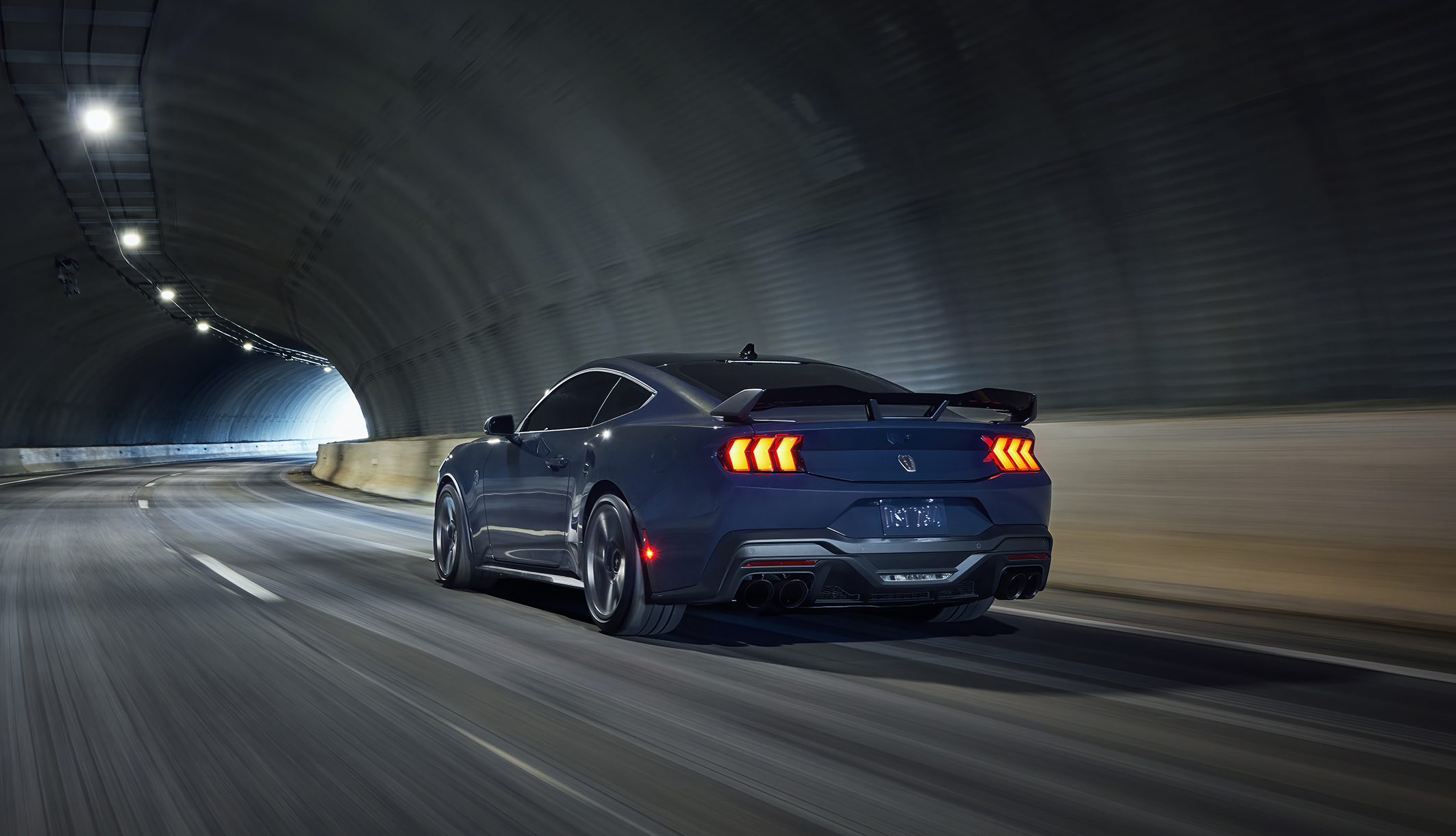 Ford Mustang Dark Horse azul visto da diagonal traseira em movimento em um túnel. 