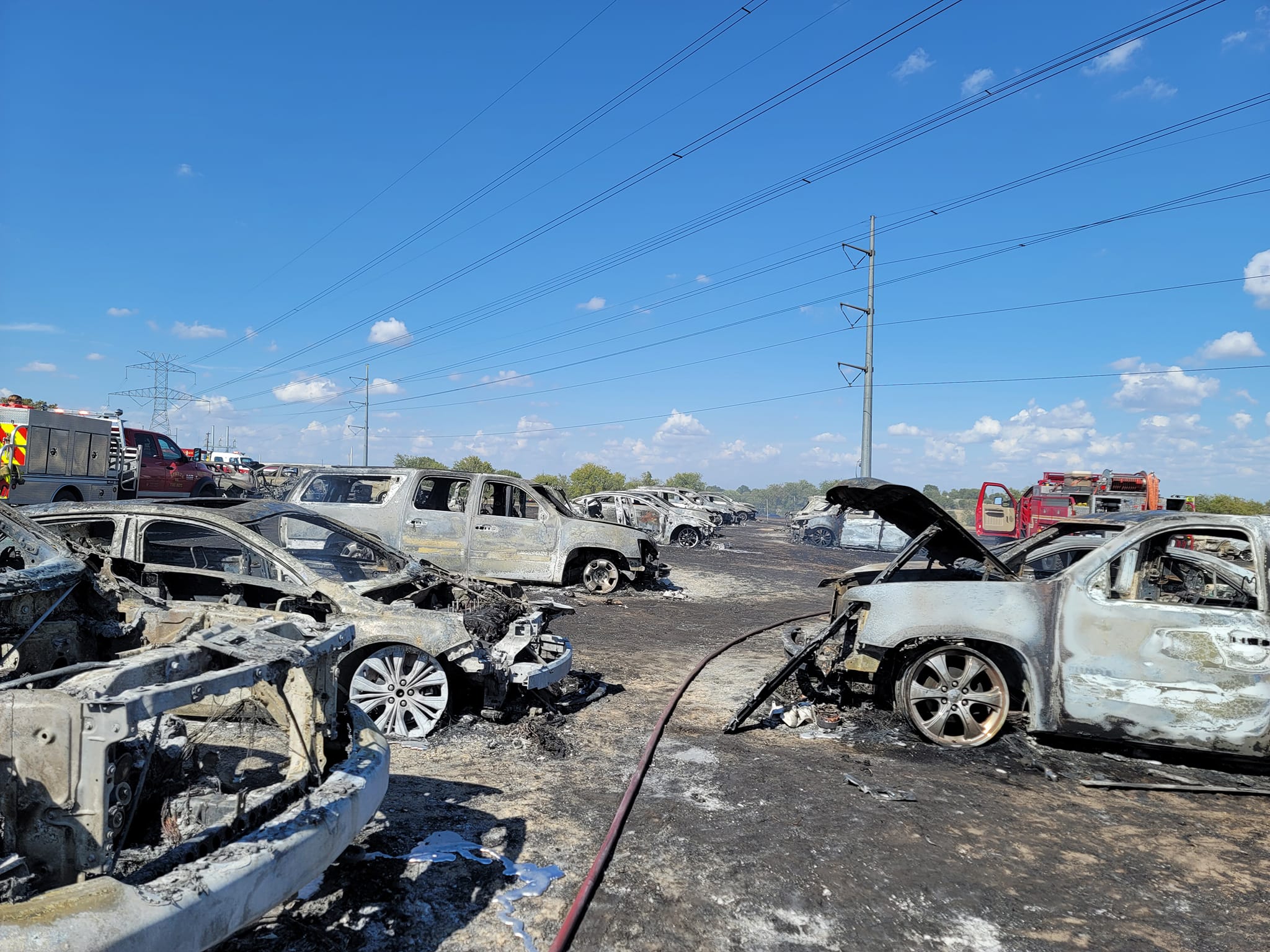 Visão do estacionamento da fazenda com vários carros destruídos e queimados. 