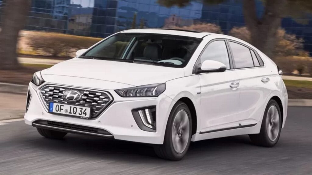 Hyundai Ioniq branco visto da diagonal frontal em movimento na rua. Ele possui o mesmo motor do Kona híbrido.