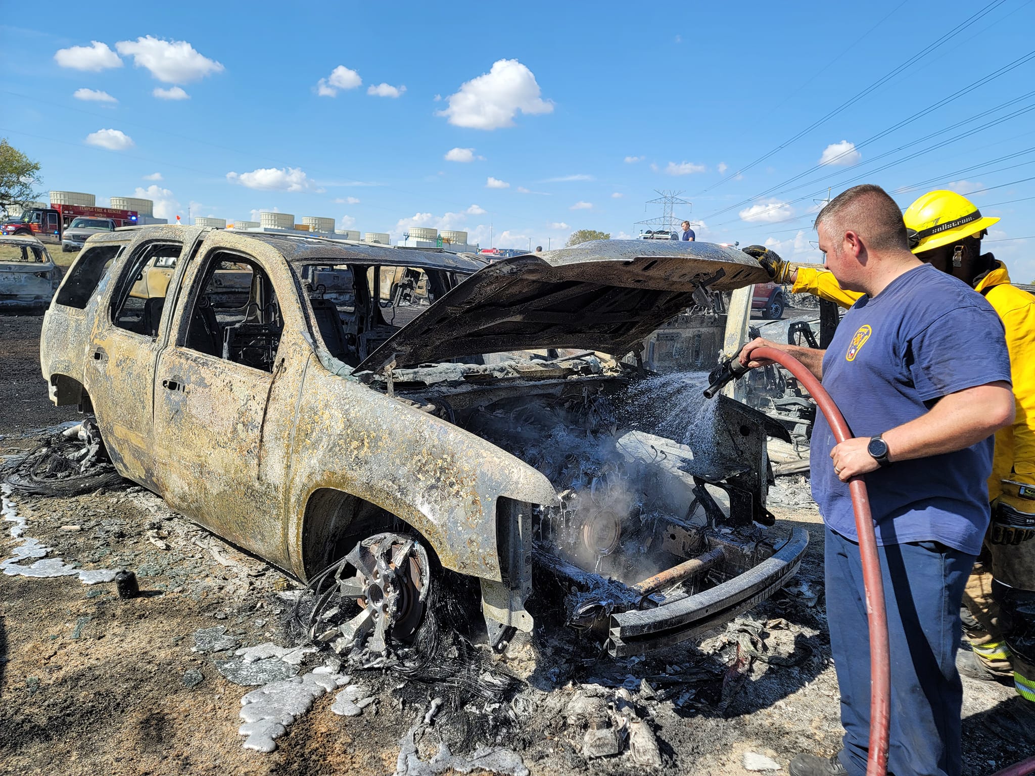 Bombeiro jogando água através de mangueira em um carro totalmente destruído. 