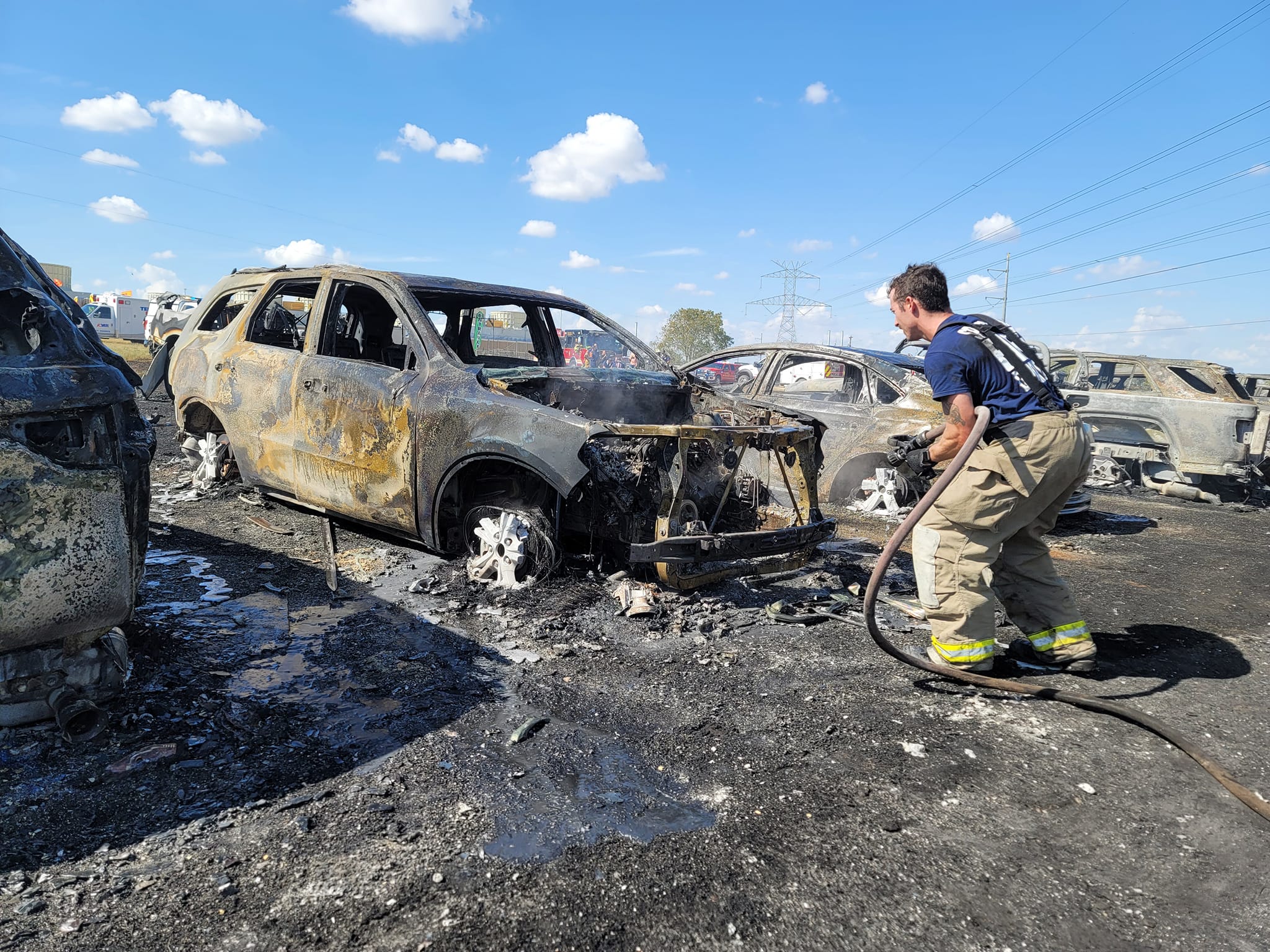 Bombeiro jogando água através de mangueira em um carro totalmente destruído. 