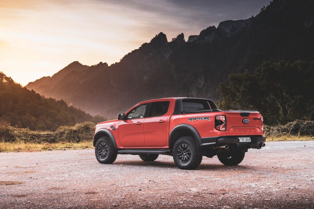 Ford Ranger Raptor laranja em chão de terra e vista da diagonal traseira.