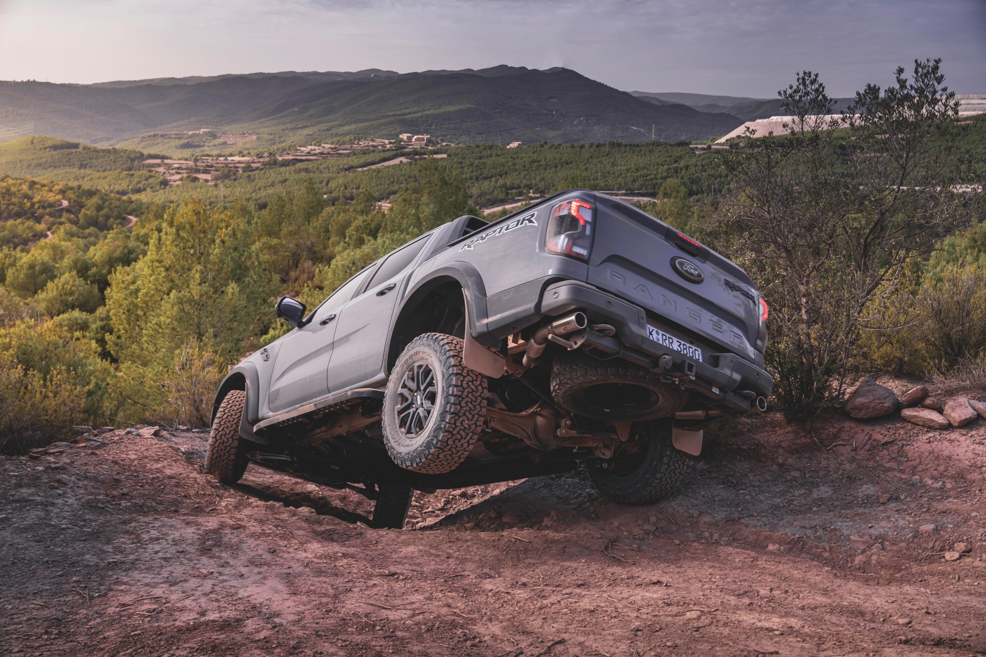 Ford Ranger Raptor cinza vista da diagoanal traseira descendo uma ladeira. O pneu traseiro da esquerda está suspenso.