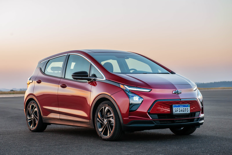 Chevrolet Bolt EV vermelho visto da diagonal frontal estacionado em chão de asfalto.