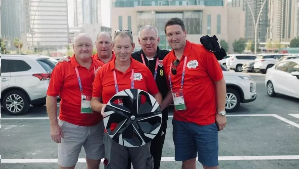 Quatro homens de vermelho posam com roda de carro na mão.