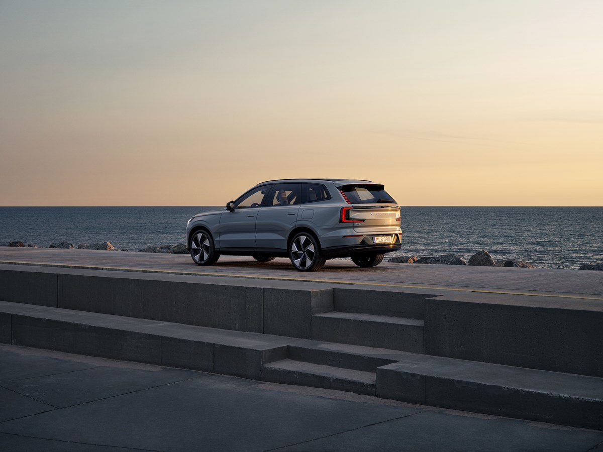 Volvo EX90 cinza visto da diagonal traseira. Atrás dele, há paisagem com mar.