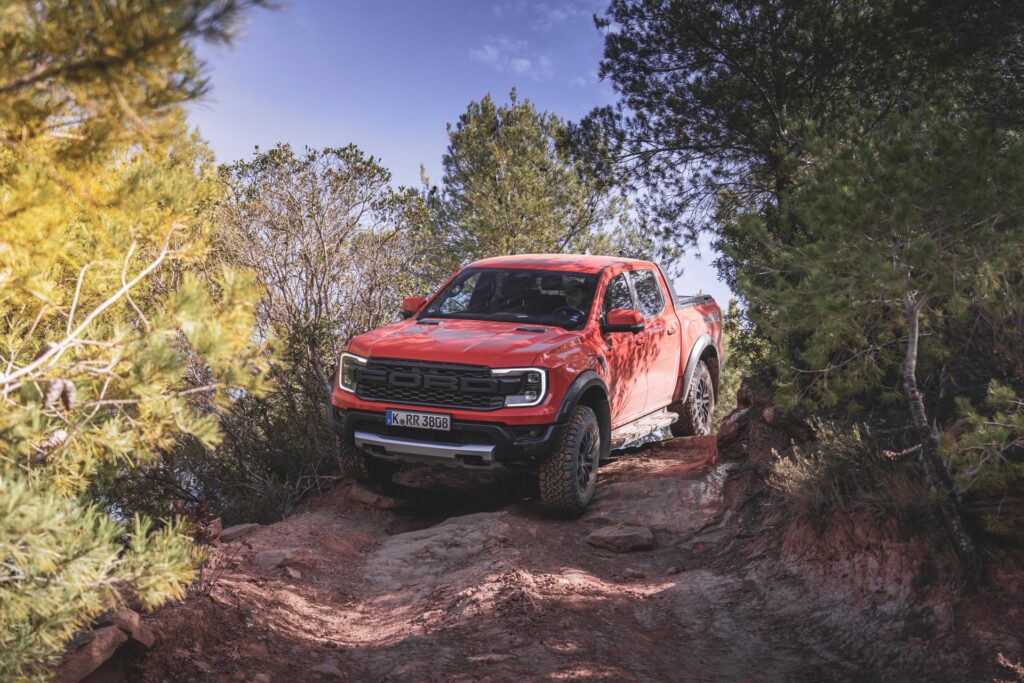 Ford Ranger Raptor laranja vista da diagonal frontal descendo ladeira de terra.