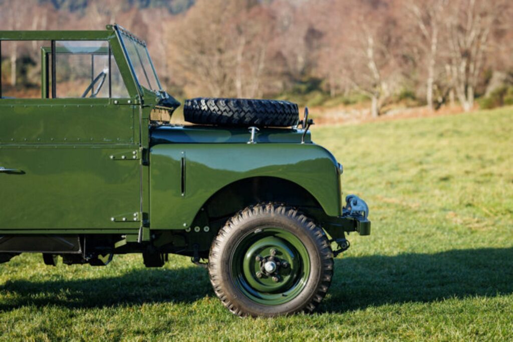 Parte da frente do Land Rover Série 1 do Rei George VI verde. Ela é vista da diagonal frontal em um campo de grama.