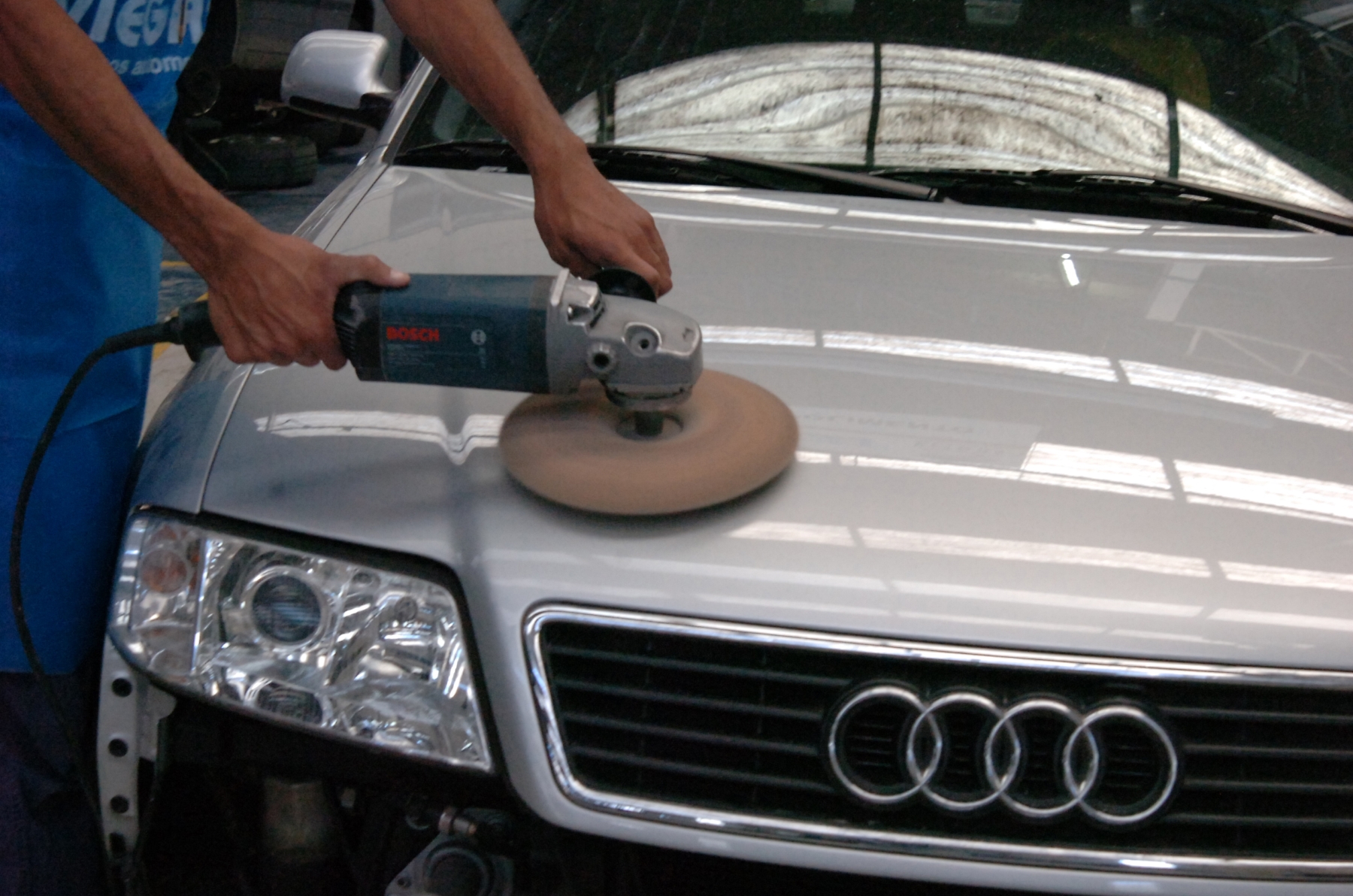 Polimento de pintura feito em modelo Audi em oficina homem com máquina de polir; para matéria de cuidados com o carro em dias de calor extremo.