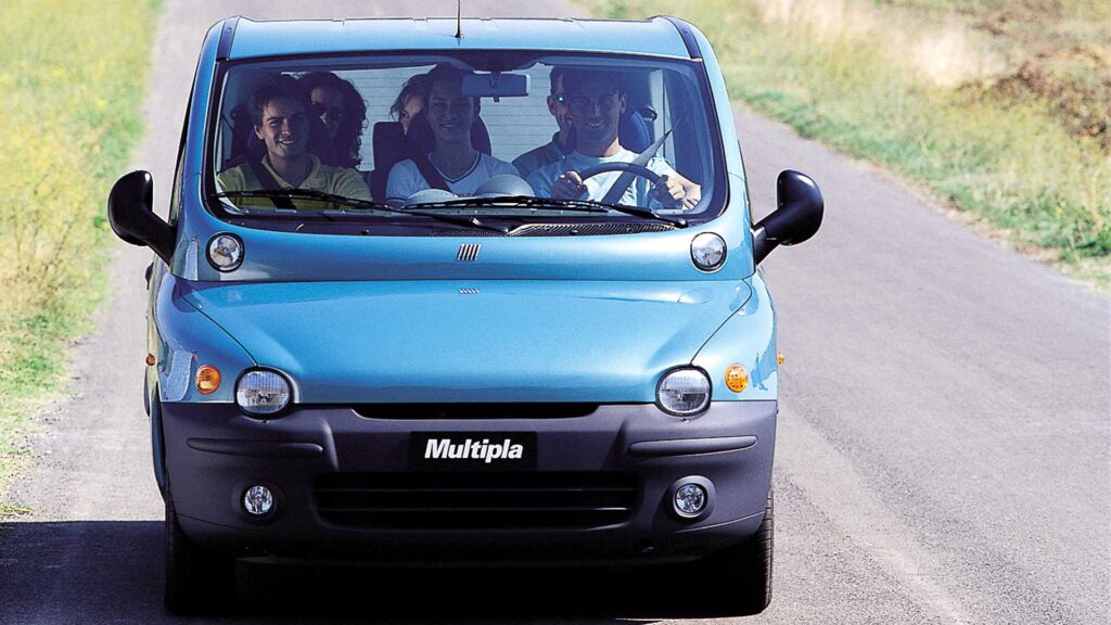 Fiat Multipla azul visto de frente em movimento na estrada. Há três ocupantes na fileira de bancos dianteira do carro.