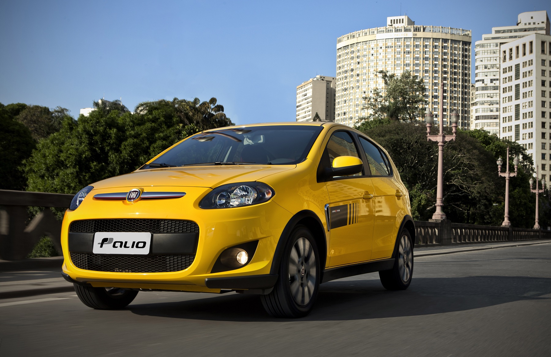 Fiat Palio Sporting amarelo 2012 de frente em movimento com paisagem urbana ao fundo