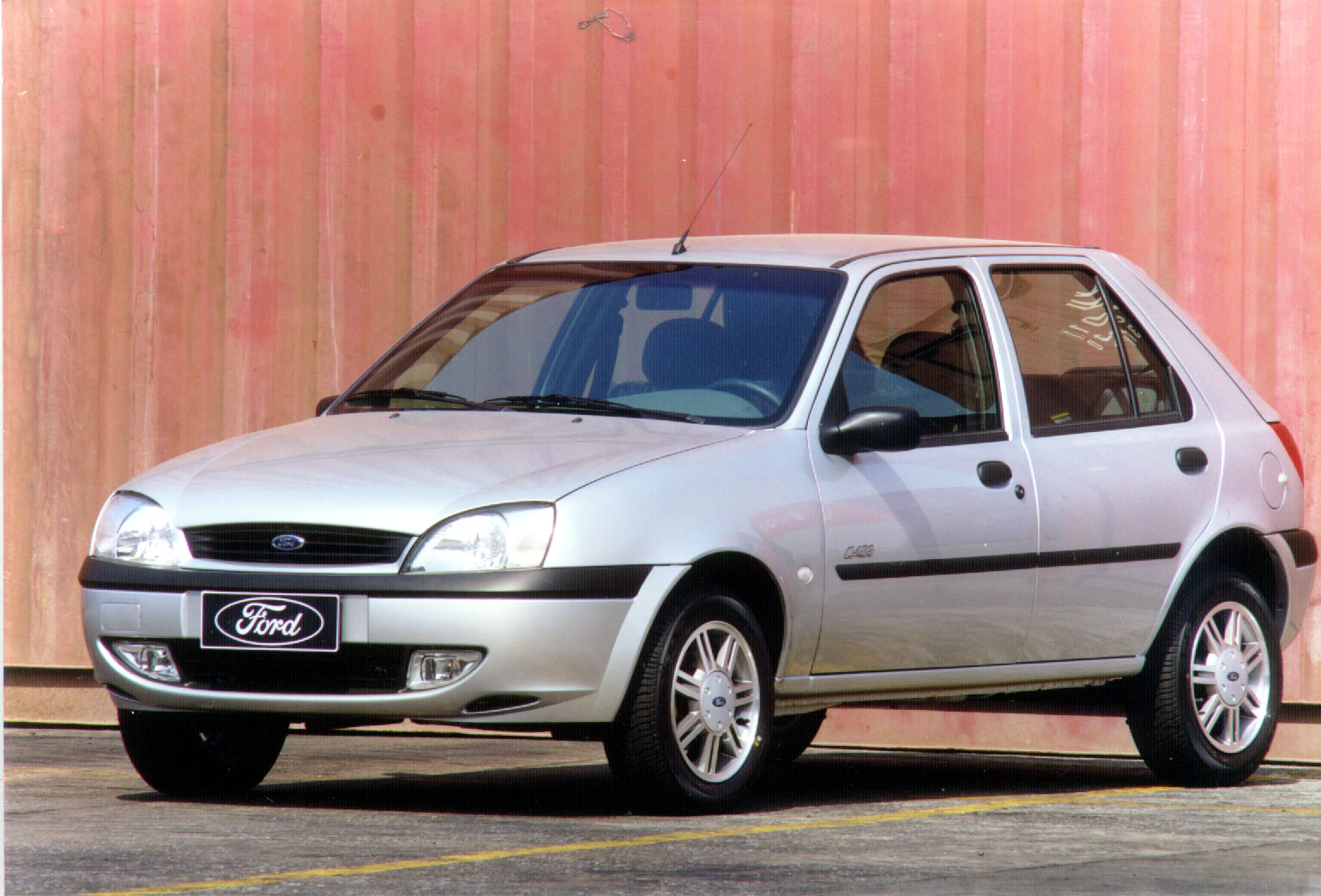 Ford Fiesta ano 2000 prata visto de frente e estacionado