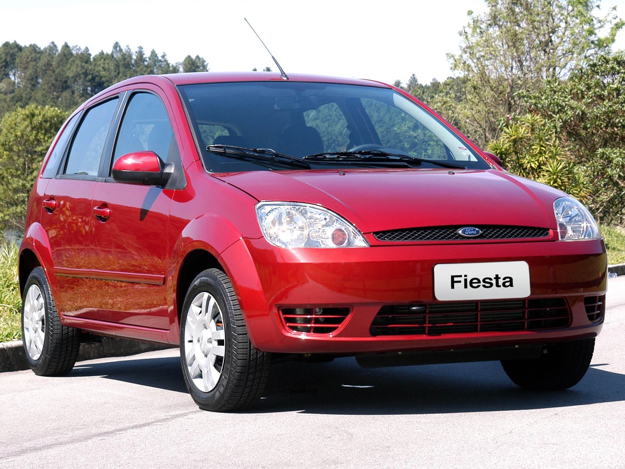 Ford Fiesta ano 2003 vermelho visto de frente e estacionado