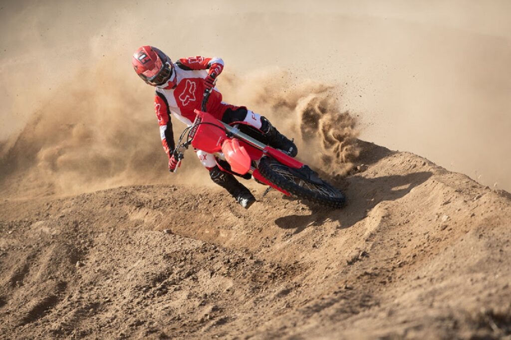 Piloto manobrando uma Honda CRF em ladeira de areia. 