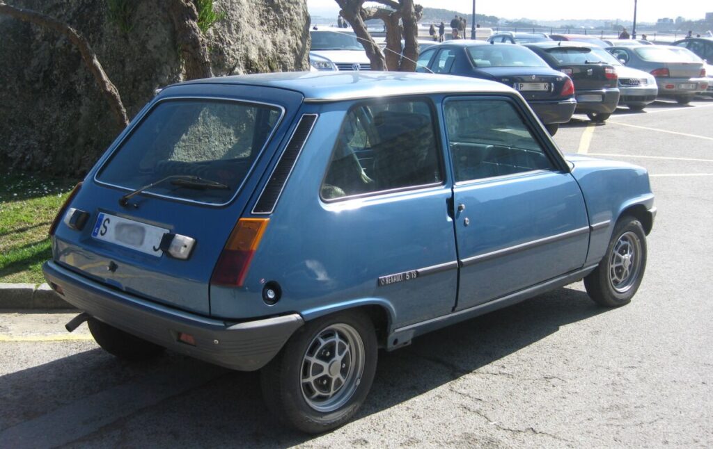 Renault 5 em tom azul visto da diagonal traseira estacionado.