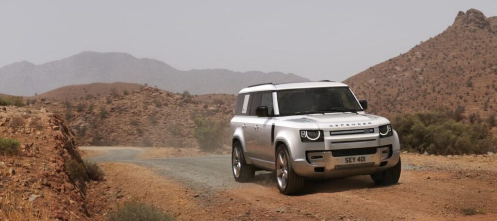 Novo Land Rover Defender 130, visto da diagonal frontal, em movimento na estrada de terra.