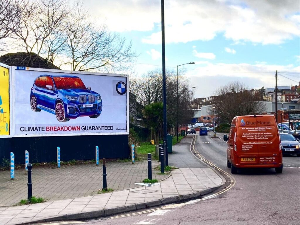 Outdoor subvertido com mensagem de ataque à BMW. A frase diz "Colapso climático garantido".