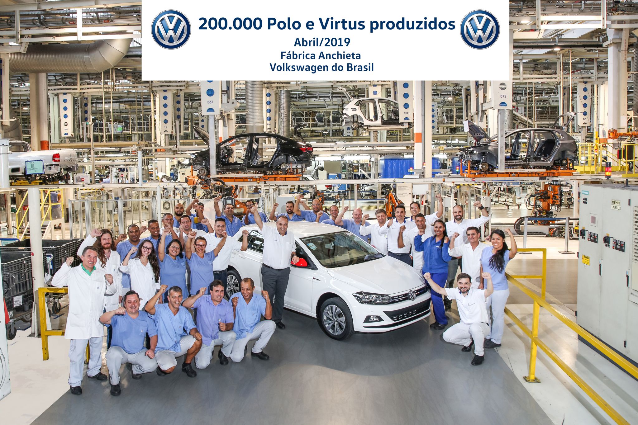 Pessoas posando ao lado de veículo dentro de fábrica da Volkswagen. Elas estão sorrindo e comemoram o feito de 200.000 modelos de Polo e Nivus produzidos. Há uma placa com esse feito descrito