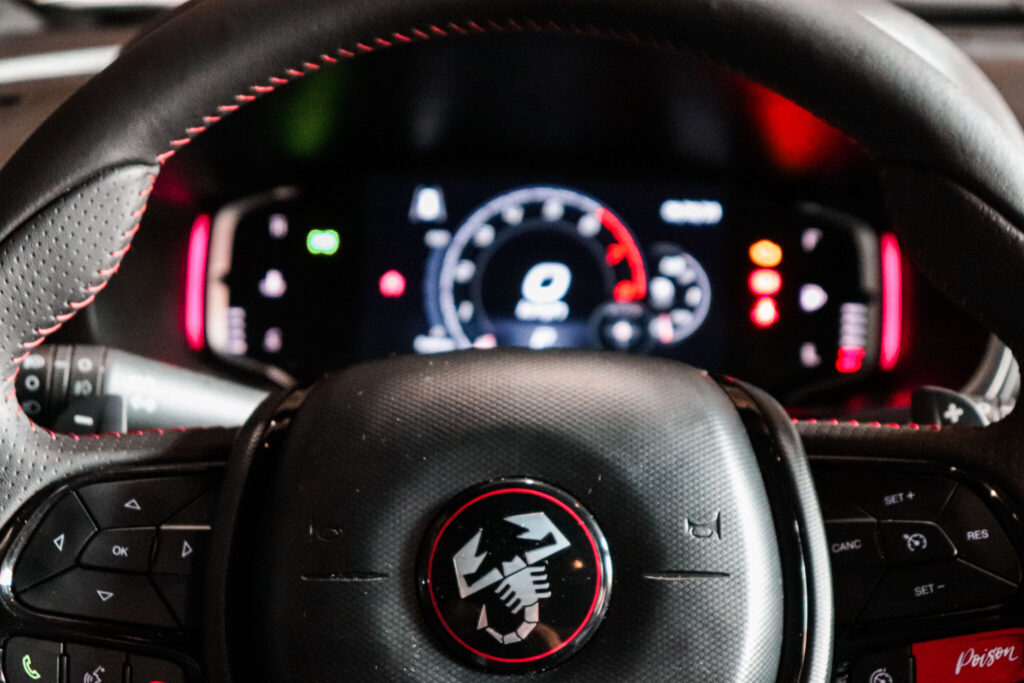 Detalhes do volante do Pulse Abarth, mostrando o escorpão no centro do volante e as teclahs multifuncionais e o painel desfocado ao fundo