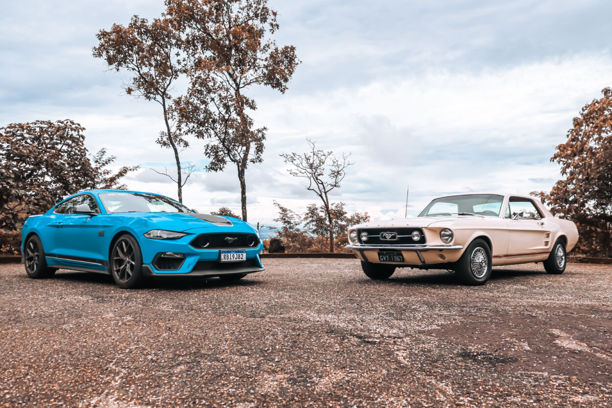 Mustang Mach 1 2022 azul estacionado ao lado de Ford Mustang GT 1967, ambos vistos de frente