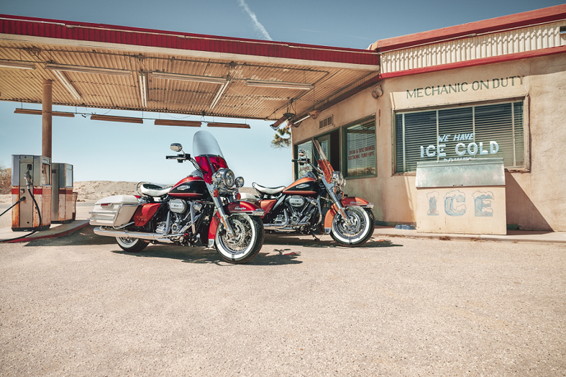 harley davidson electra glide highway king vermelha e laranja de lateral estaticas no posto de combustivel