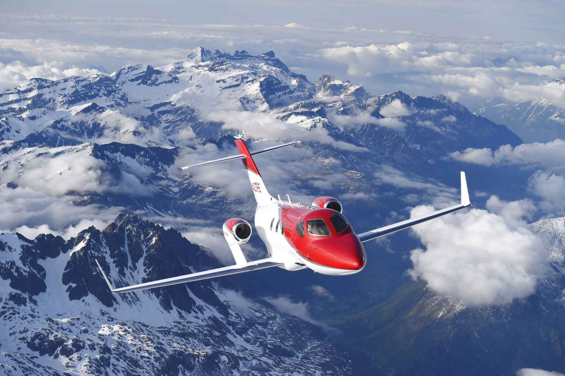 HA-420 HondaJet vermelho e branco sobrevoando montanhas com neve ; para matéria sobre marcas de carro com investimentos inusitados