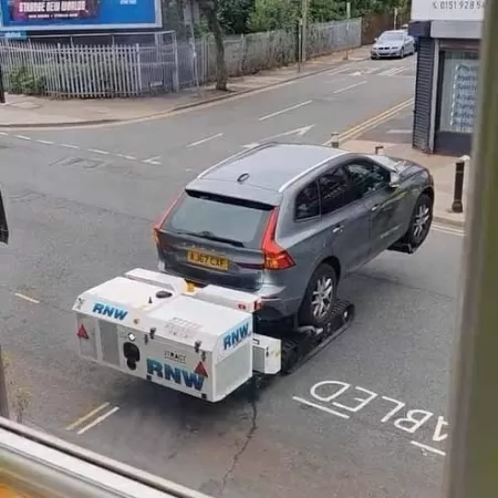 Robô reboque reboca carro cinza em rua apertada em Londres.